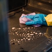 Hand met rubberen handschoen veegt de binnenkant van een oven schoon met een sopdoek