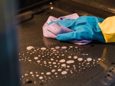 Hand met rubberen handschoen veegt de binnenkant van een oven schoon met een sopdoek