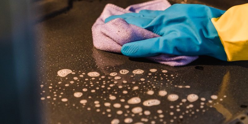 Hand met rubberen handschoen veegt de binnenkant van een oven schoon met een sopdoek